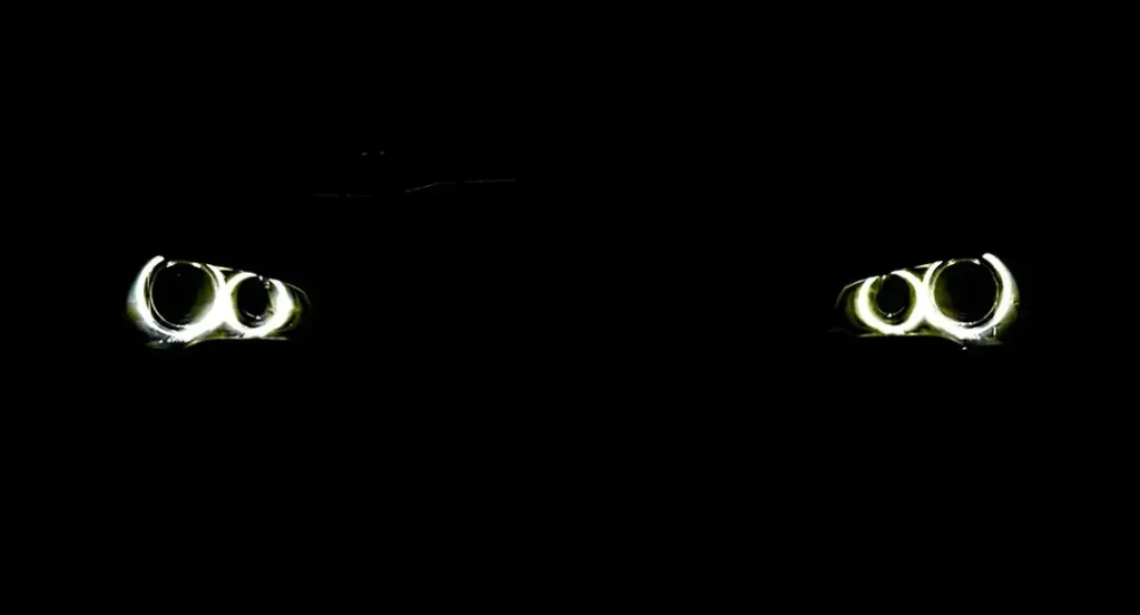 Two angel eye projector headlights glowing in a pitch-black night scene