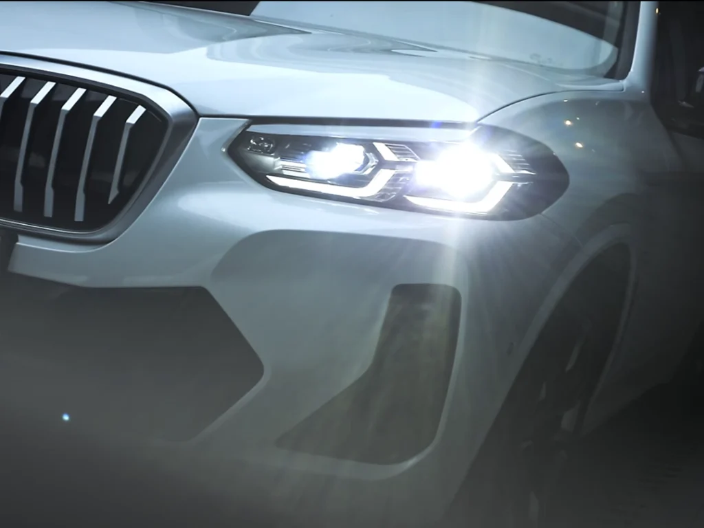 Night road view of a BMW using LED projector headlamps, showing a sharp low-beam cutoff and even beam pattern.