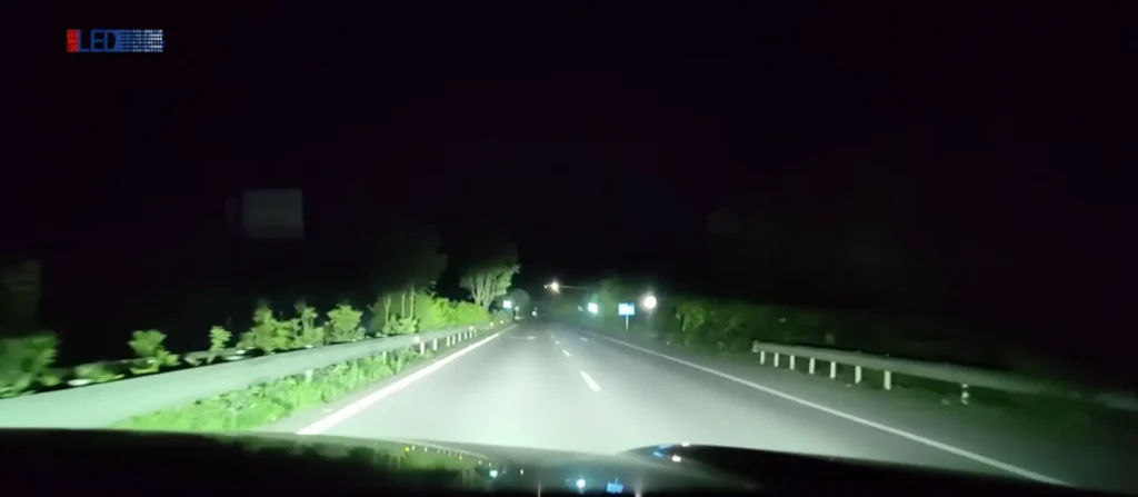 Dashcam photo on a dark highway with headlight projector lens activated, showing brighter forward illumination