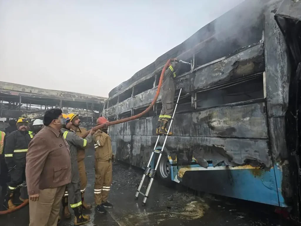 Firefighters work at the crash site beside a burned bus on the Delhi–Agra Expressway after a fog-related pileup; fog lights and fog lights car visibility are critical in low visibility.