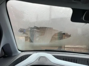 منظر القيادة المسائية الممطرة في المساء مع زجاج أمامي غير واضح ومرآة جانبية مبللة؛ مصباح ضباب لصيانة رؤية السيارة.