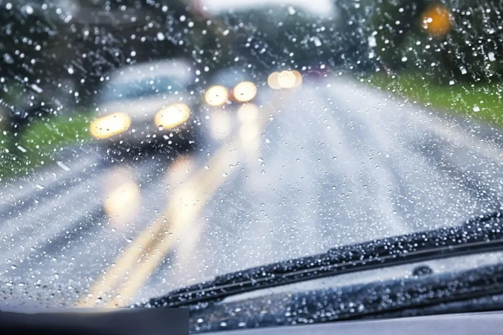 Driver’s view in rain with water on the windshield and wipers working; fog lamp for car visibility maintenance starts with clear glass.