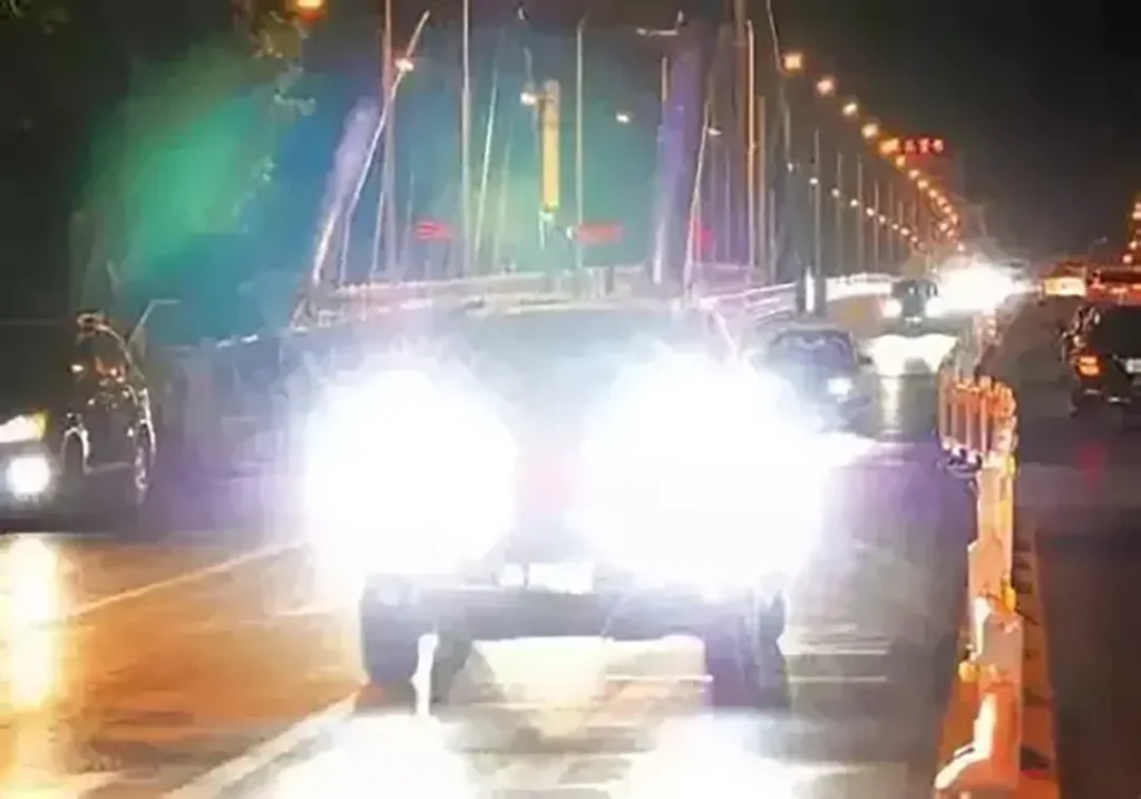 A vehicle driving on a public road with overly bright forward-facing lights causing glare, illustrating why many regions emphasize brightness, aim, and glare control in exterior lighting enforcement.