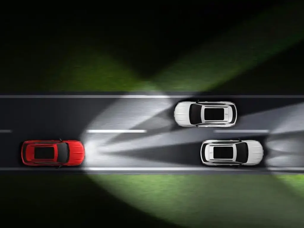 Night road scene showing projector headlights with Adaptive Driving Beam (ADB), adjusting the light pattern around oncoming traffic and vehicles ahead.
