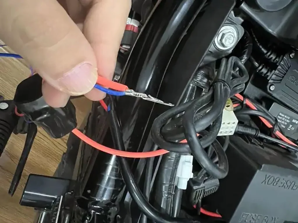 Engine bay close-up showing relay, inline fuse, and wiring harness installed to wire spotlights on a car