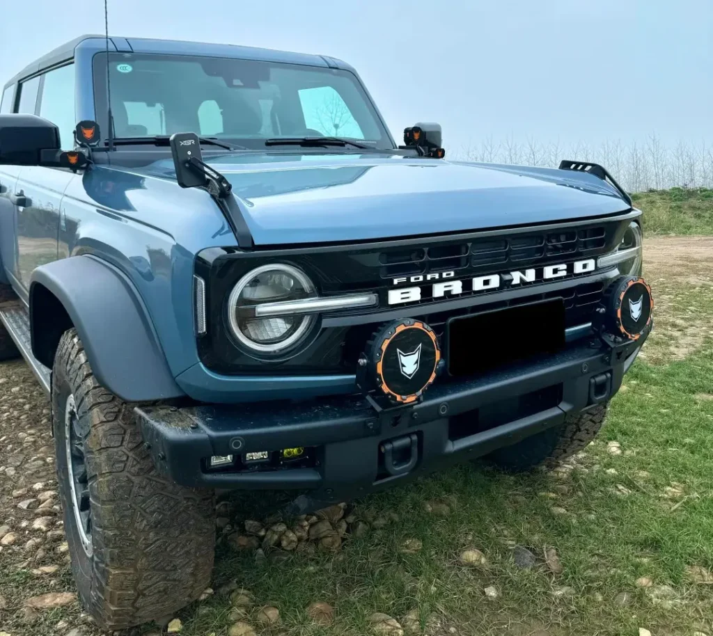 Ford Bronco with car spotlights mounted in front of the side mirrors lighting a dark road at night