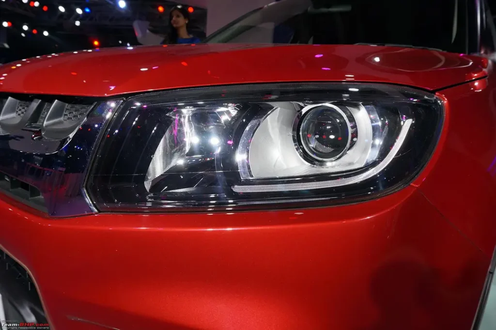 Close-up of the projector headlights on a red Vitara Brezza, highlighting the projector lens and headlight housing.