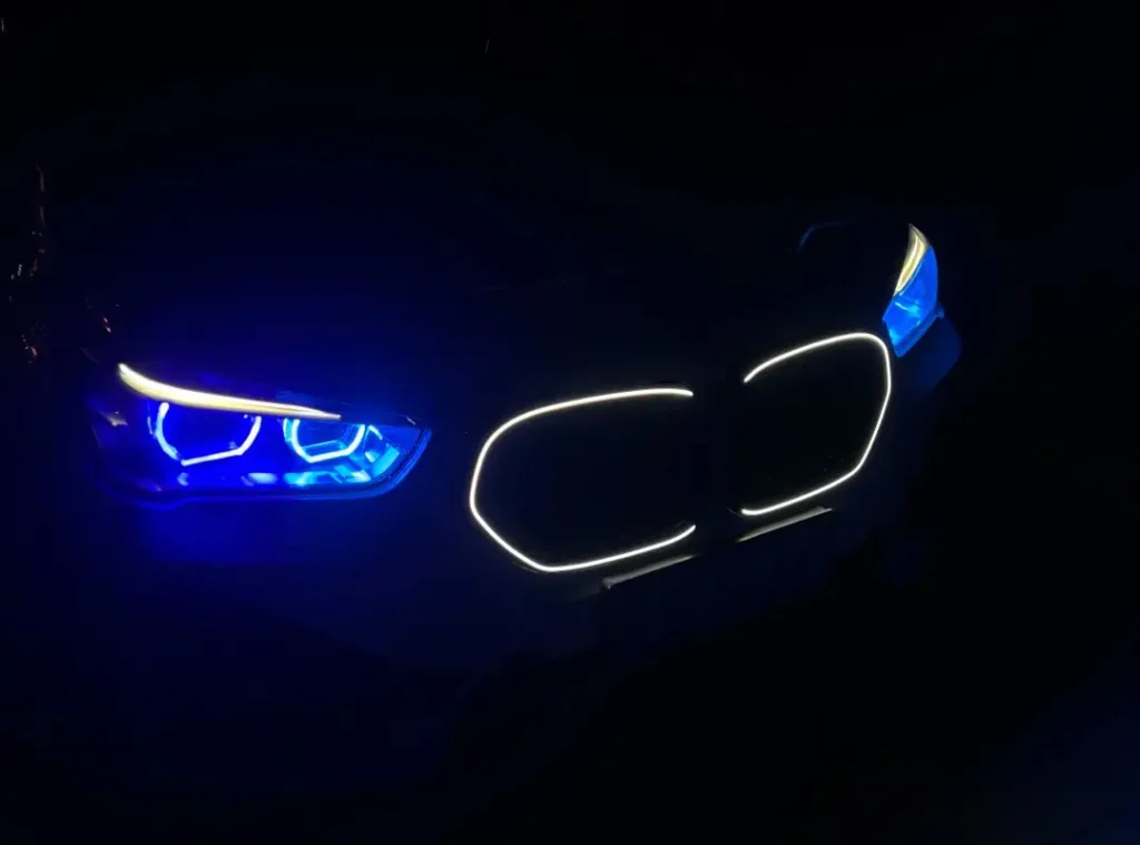 BMW vehicle with white grille LED lights and blue ambient headlights, photographed at night