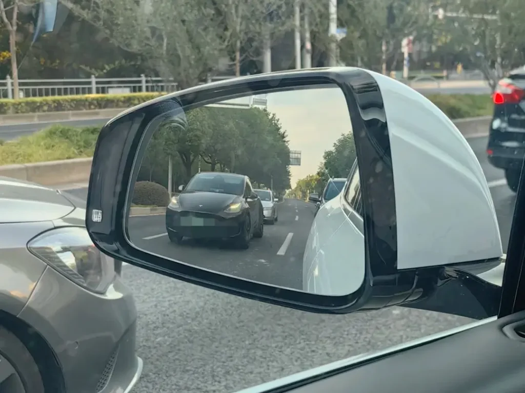 rear vehicle visible in car side mirror with blind spot warning light still off showing spot lights available safety system